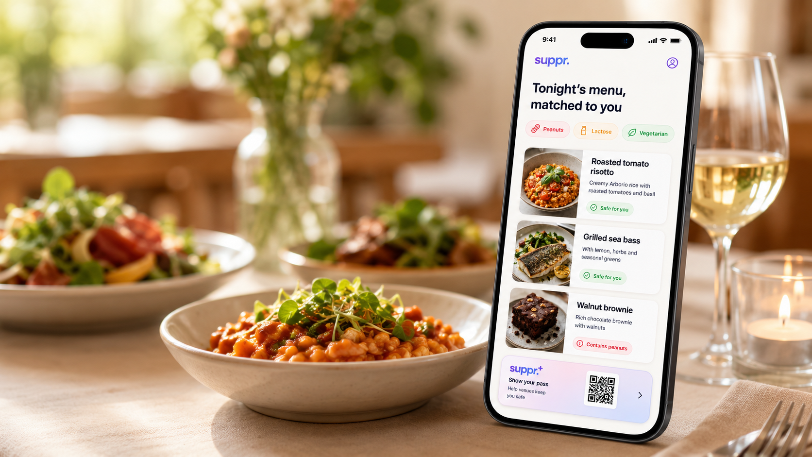 A sunlit restaurant table with fresh dishes and a glass of wine, and a phone standing upright showing the Suppr app: tonight's menu matched to a diner's profile, dishes marked safe for you or flagged for peanuts, and a QR pass to show venues.