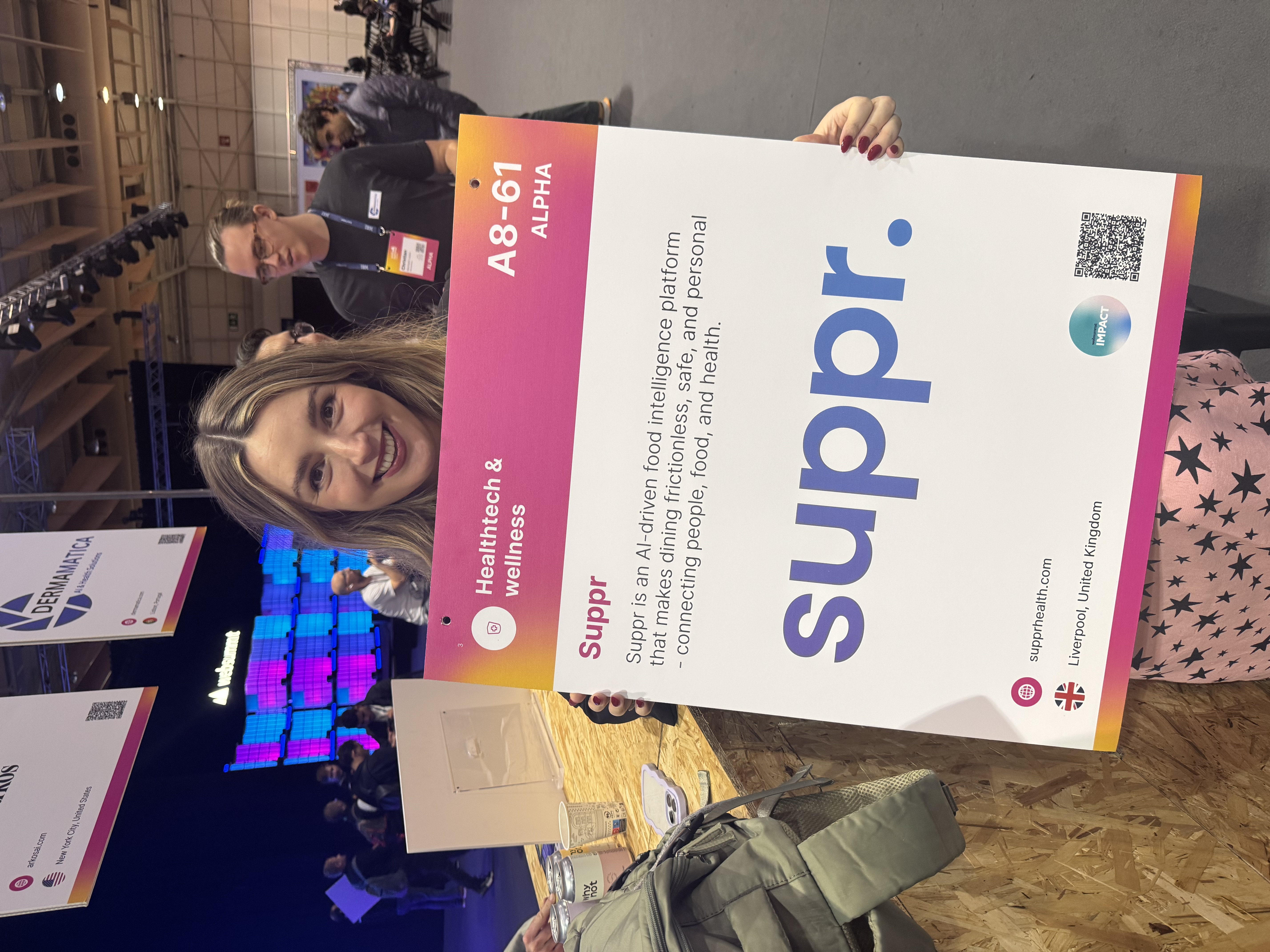A member of the Suppr team at Web Summit Alpha 2025 in Lisbon, holding the Suppr stand sign in the Healthtech and wellness category.